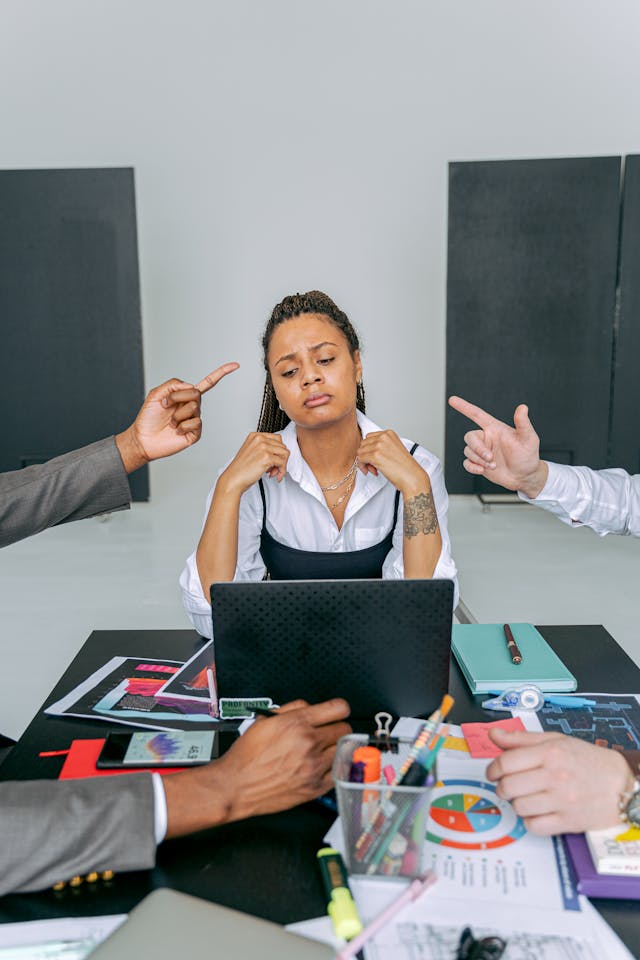 Sad woman at work table with arguing coworkers